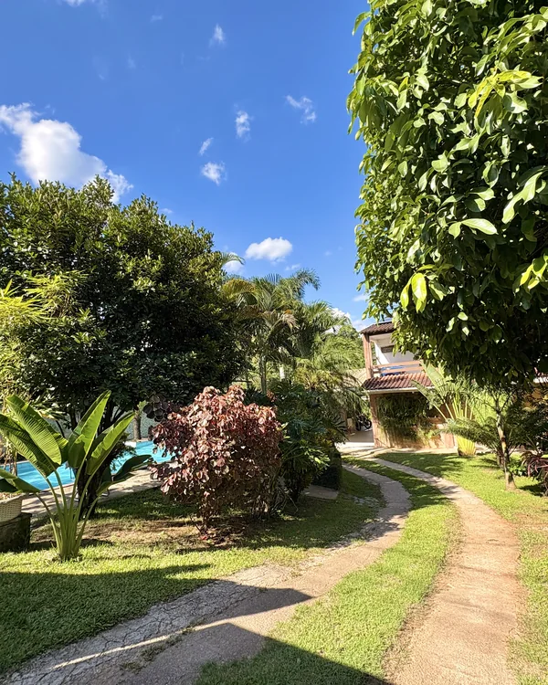 Caminho pelo gramado e pelo jardim, com piscina e construção ao fundo.