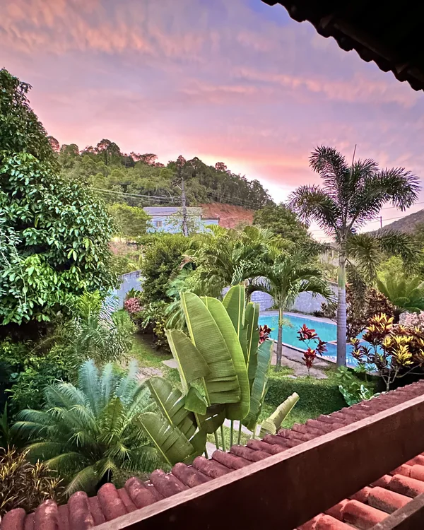 Vista da varanda para o jardim e a piscina sob um céu rosado.